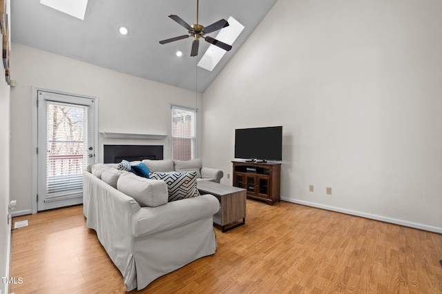 living room featuring a ceiling fan, a skylight, light wood-style flooring, and a fireplace