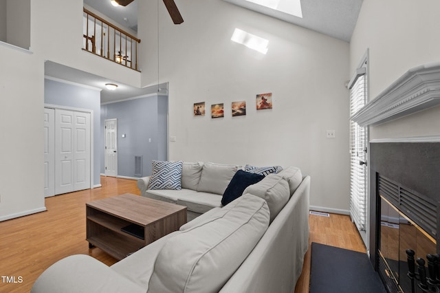 living area with baseboards, wood finished floors, a glass covered fireplace, high vaulted ceiling, and a ceiling fan