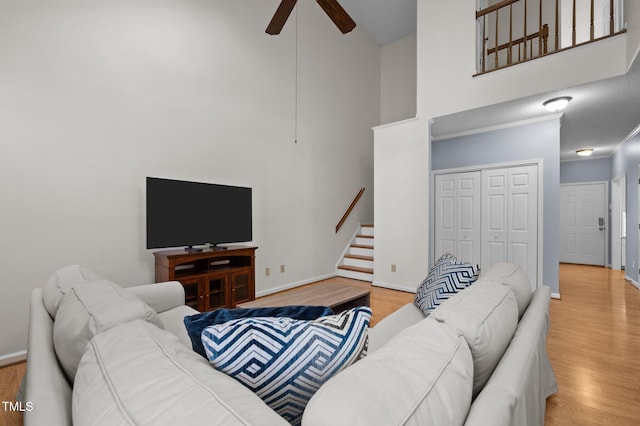 living room featuring baseboards, ceiling fan, stairs, a towering ceiling, and wood finished floors