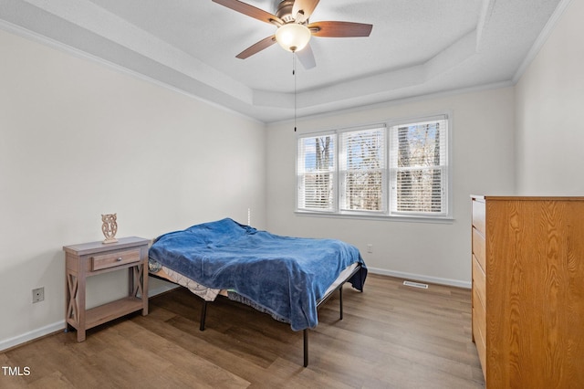 bedroom featuring baseboards, light wood-style floors, and a tray ceiling