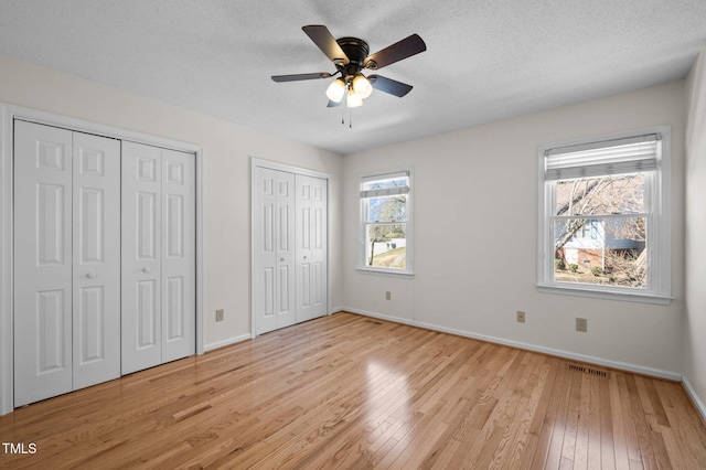 unfurnished bedroom featuring baseboards, visible vents, light wood-style floors, a textured ceiling, and two closets