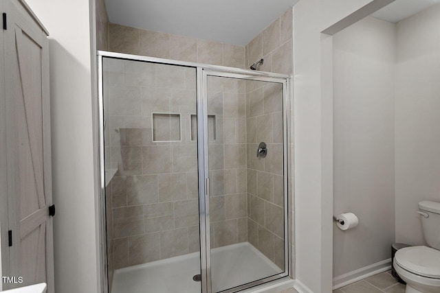 bathroom featuring tile patterned flooring, a stall shower, toilet, and baseboards