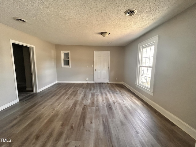 unfurnished room with dark wood-style floors, baseboards, visible vents, and a textured ceiling