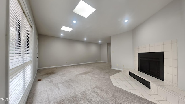 unfurnished living room featuring baseboards, carpet, recessed lighting, a tile fireplace, and a skylight