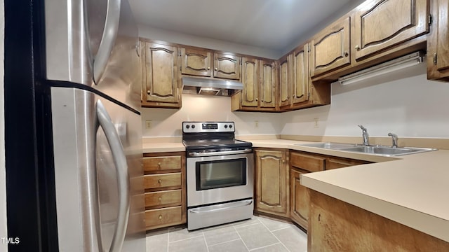 kitchen with under cabinet range hood, light countertops, light tile patterned floors, stainless steel appliances, and a sink