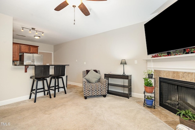 sitting room featuring light carpet, ceiling fan, a fireplace, and baseboards