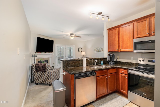 kitchen with a sink, open floor plan, a peninsula, appliances with stainless steel finishes, and a tile fireplace