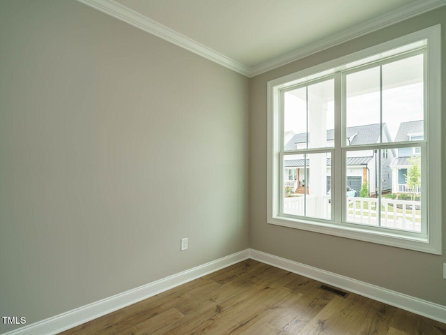 spare room with ornamental molding, visible vents, baseboards, and wood finished floors