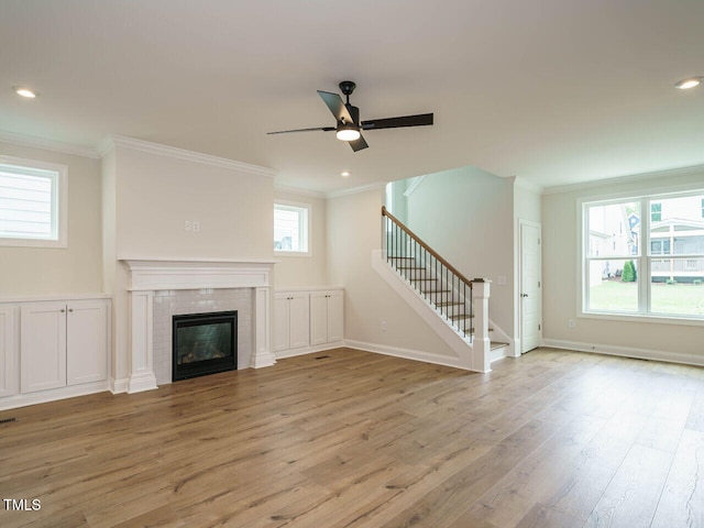 unfurnished living room with baseboards, stairs, ornamental molding, light wood-type flooring, and a glass covered fireplace