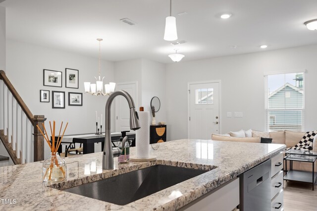 kitchen with light stone counters, plenty of natural light, stainless steel dishwasher, and a sink