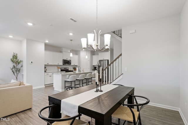 dining room with stairs, an inviting chandelier, baseboards, and light wood-type flooring