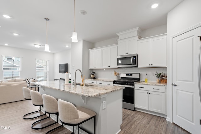 kitchen featuring light wood-type flooring, a sink, tasteful backsplash, open floor plan, and appliances with stainless steel finishes