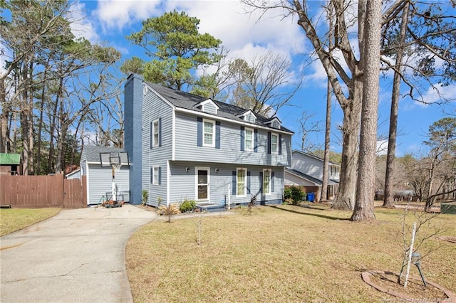 colonial-style house with a chimney, fence, a front lawn, and concrete driveway