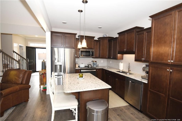 kitchen featuring appliances with stainless steel finishes, a kitchen island, a sink, wood finished floors, and a kitchen bar