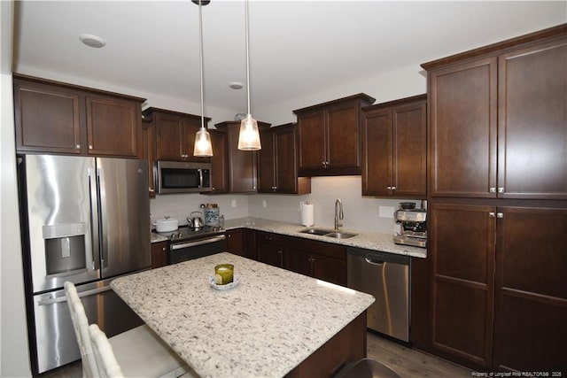 kitchen with a center island, appliances with stainless steel finishes, dark brown cabinetry, light stone countertops, and a kitchen breakfast bar