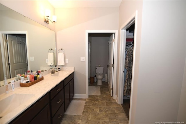 full bathroom featuring a walk in closet, a sink, baseboards, and double vanity