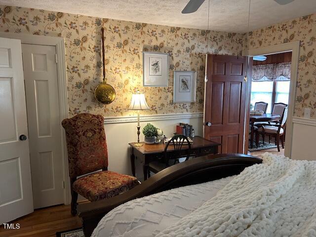 bedroom featuring wallpapered walls, a textured ceiling, wood finished floors, and wainscoting