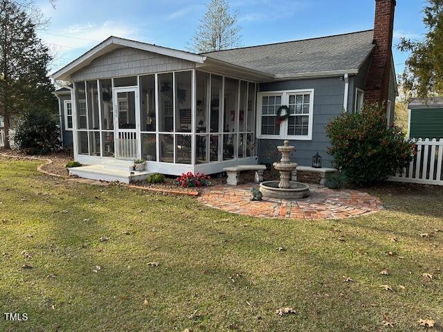 rear view of house with a lawn, a chimney, a sunroom, and fence