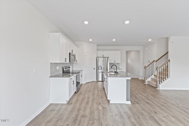 kitchen with light wood finished floors, appliances with stainless steel finishes, a sink, and white cabinets