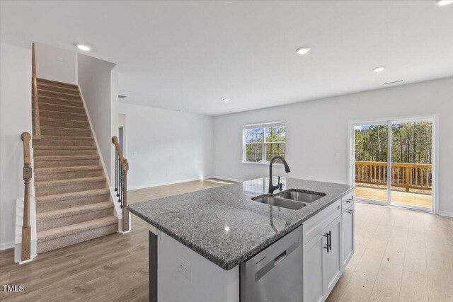 kitchen with light wood finished floors, white cabinets, a sink, dark stone countertops, and dishwasher