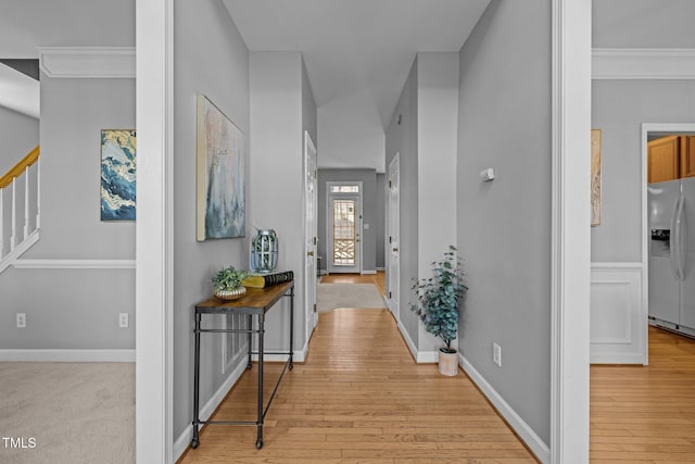 corridor featuring stairs, baseboards, light wood-type flooring, and ornamental molding