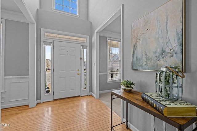 foyer with light wood-style flooring, a high ceiling, and ornamental molding