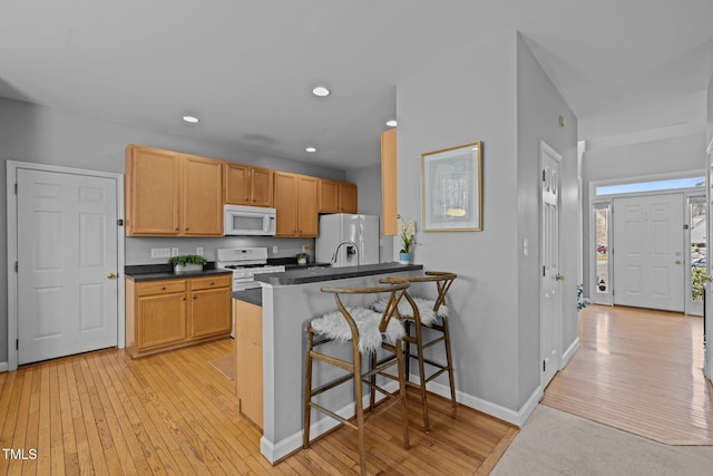 kitchen with a breakfast bar, light wood-style flooring, dark countertops, recessed lighting, and white appliances