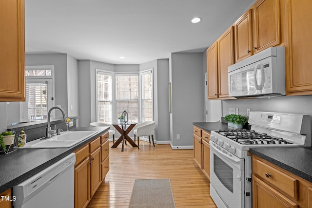 kitchen with dark countertops, light wood finished floors, baseboards, white appliances, and a sink