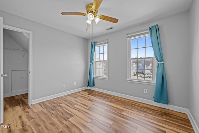 unfurnished bedroom with visible vents, a walk in closet, baseboards, and wood finished floors