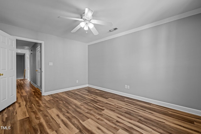 empty room with visible vents, wood finished floors, crown molding, baseboards, and ceiling fan