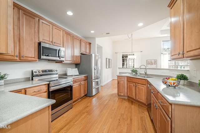 kitchen with light wood finished floors, visible vents, a peninsula, stainless steel appliances, and a sink