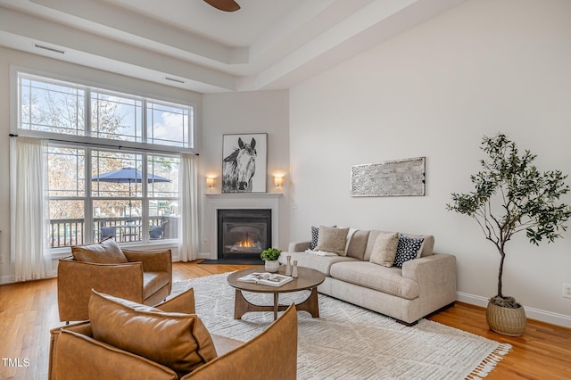 living room with a towering ceiling, baseboards, light wood-style flooring, and a fireplace with flush hearth