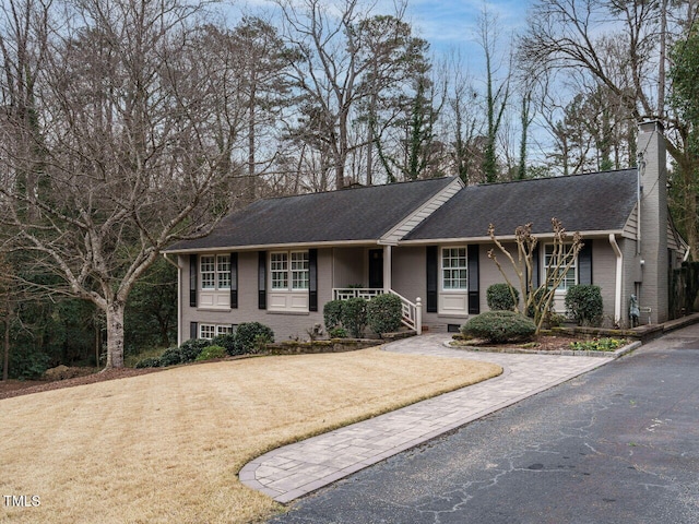 ranch-style house with brick siding, a chimney, roof with shingles, and a front yard