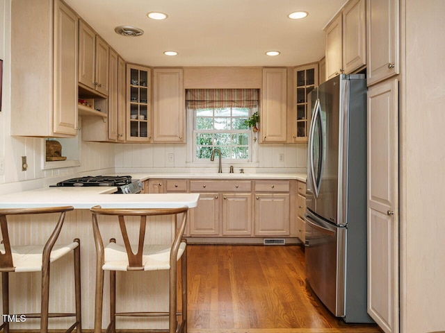 kitchen featuring visible vents, a peninsula, freestanding refrigerator, wood finished floors, and a sink