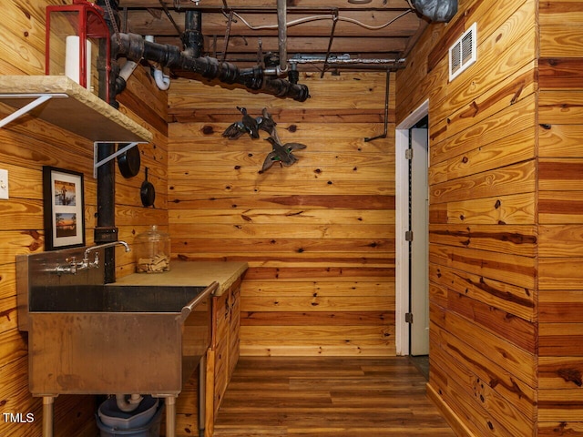 bar featuring dark wood-style floors, wood walls, and a sink