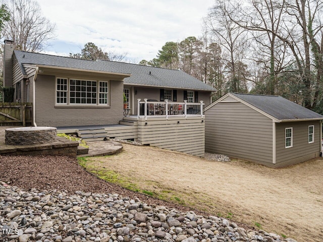 view of front of property with brick siding, a shingled roof, fence, a wooden deck, and a chimney