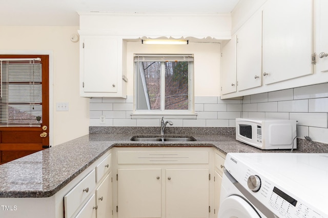 kitchen featuring a sink, washer / clothes dryer, tasteful backsplash, white cabinetry, and white microwave