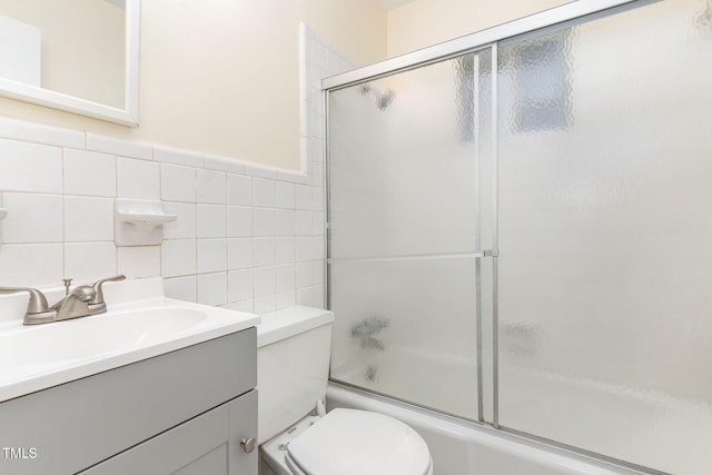 bathroom with enclosed tub / shower combo, toilet, tile walls, and vanity