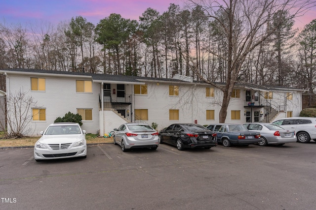 view of front of house with stairway, brick siding, and uncovered parking