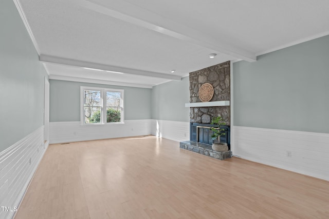 unfurnished living room featuring beamed ceiling, ornamental molding, wood finished floors, a fireplace, and wainscoting