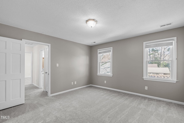 empty room featuring a wealth of natural light, visible vents, baseboards, and carpet