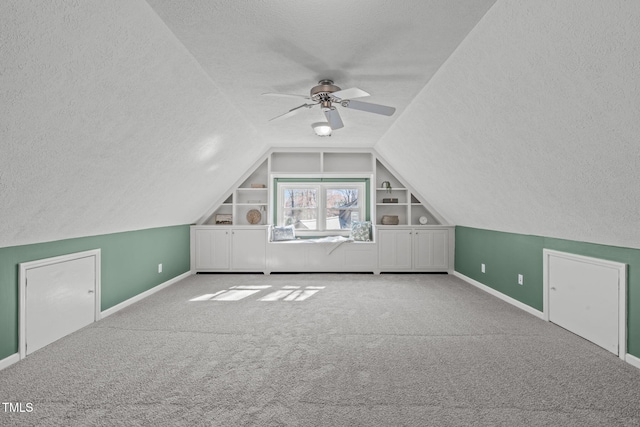 bonus room with built in shelves, a textured ceiling, lofted ceiling, and carpet flooring