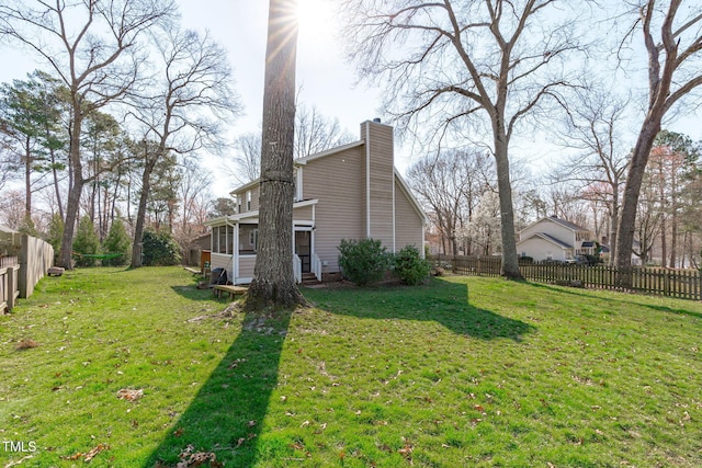 view of side of home with a lawn, a fenced backyard, a chimney, and a sunroom