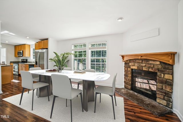 dining area featuring dark wood-type flooring, recessed lighting, a stone fireplace, and baseboards