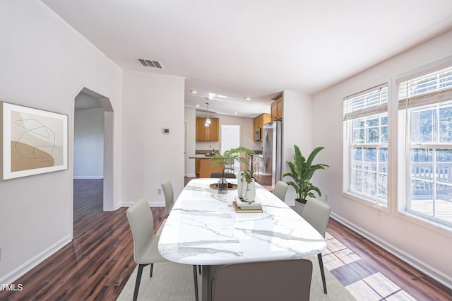 dining room featuring dark wood-style floors, baseboards, visible vents, and arched walkways