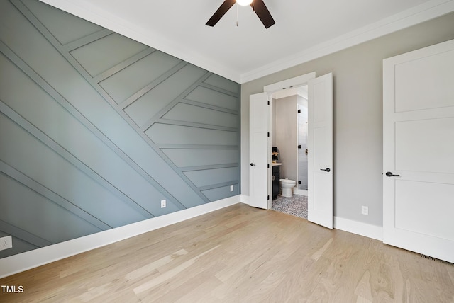 unfurnished bedroom featuring ceiling fan, baseboards, ornamental molding, ensuite bathroom, and light wood-style floors