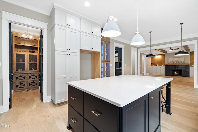 kitchen featuring white cabinetry, crown molding, light wood finished floors, and a lit fireplace