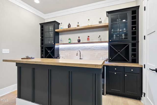 bar featuring indoor wet bar, baseboards, ornamental molding, and light wood finished floors