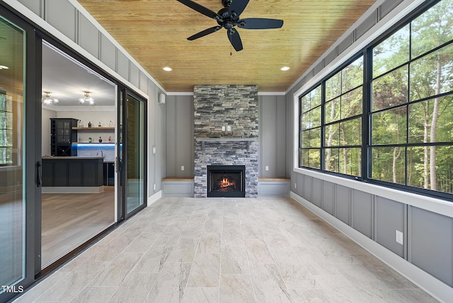 unfurnished living room with a decorative wall, wooden ceiling, a fireplace, crown molding, and ceiling fan