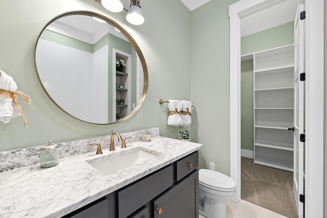 bathroom with a walk in closet, toilet, and vanity